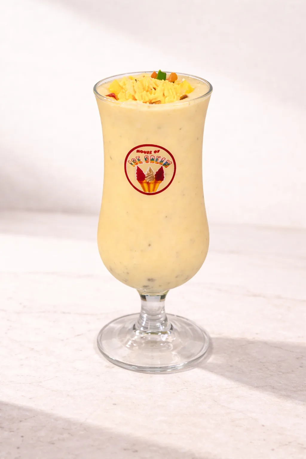 A mango falooda in a hurricane glass, topped with chopped fruit.