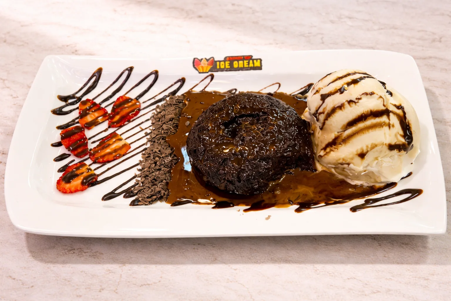 The Molten Lava Cake plated with vanilla ice cream, sliced strawberries, grated chocolate and chocolate sauce.