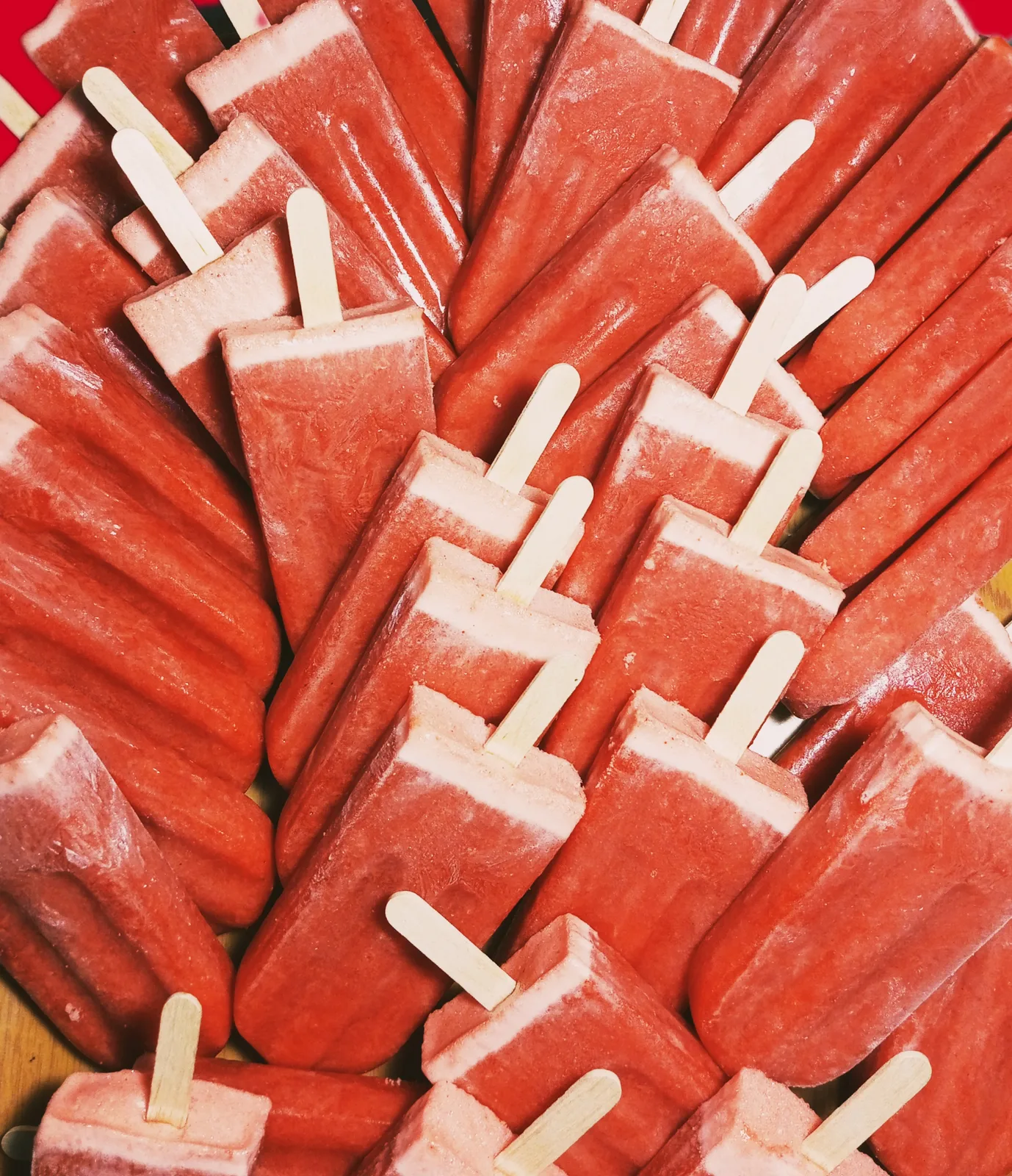 Rows of colourful handmade fruit popsicles on wooden sticks.