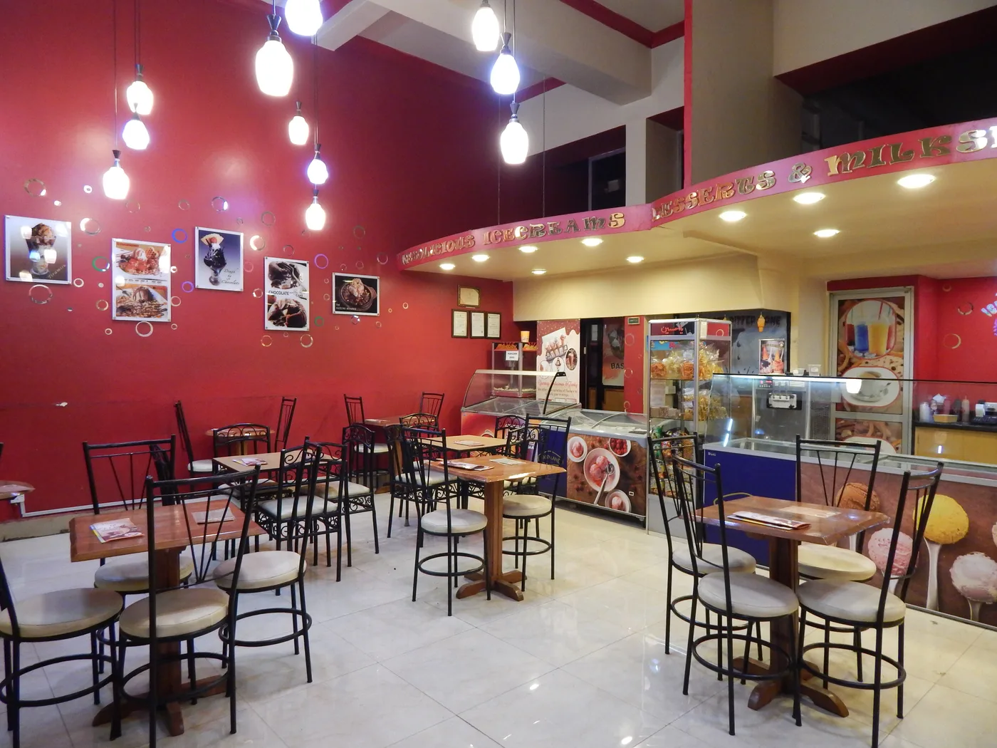 An early House of Ice Cream interior with red walls, pendant bulbs, metal-framed chairs and dessert photographs above the counter.